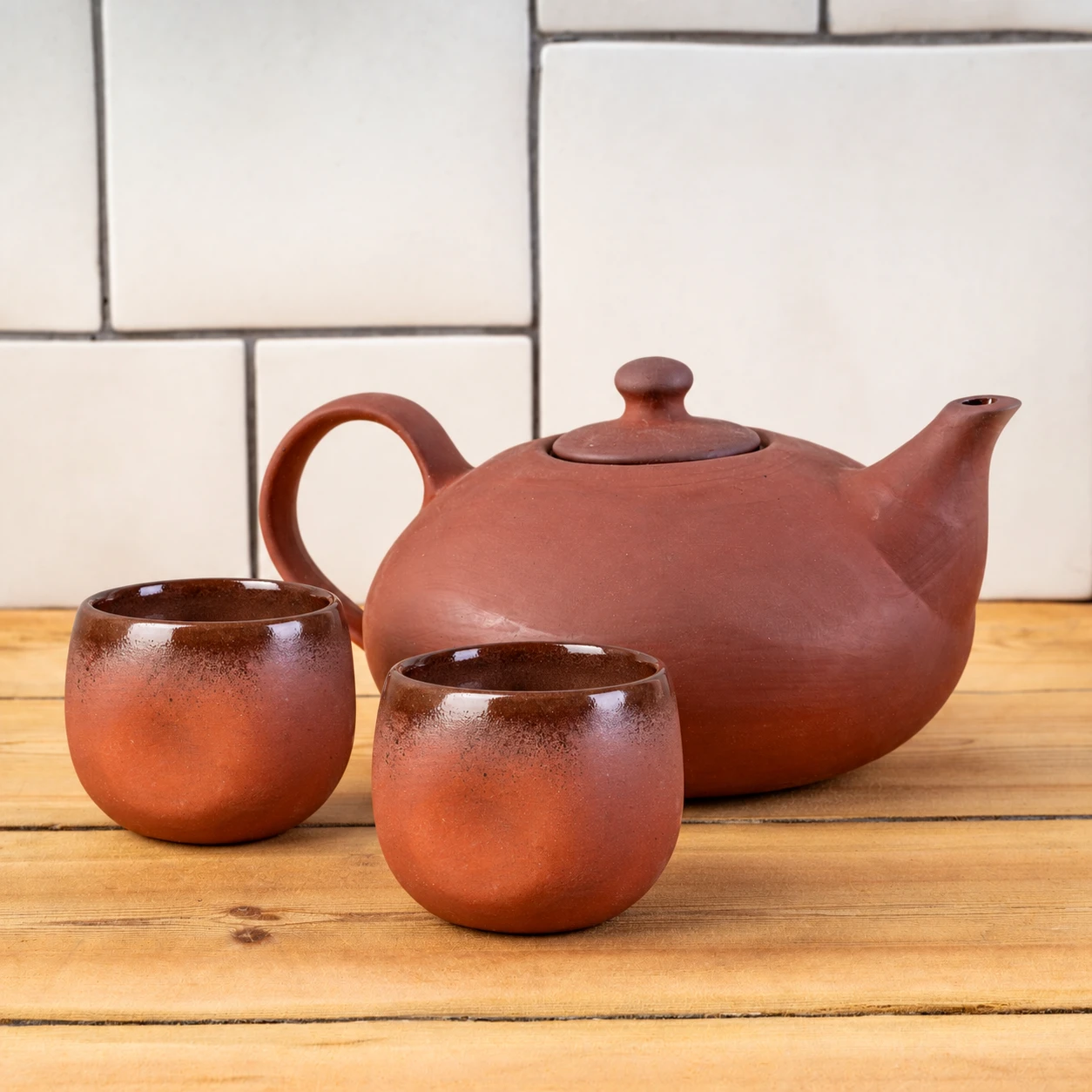 A terracotta Jupiter teapot with two dark terracotta Edith mugs on a rustic wooden table